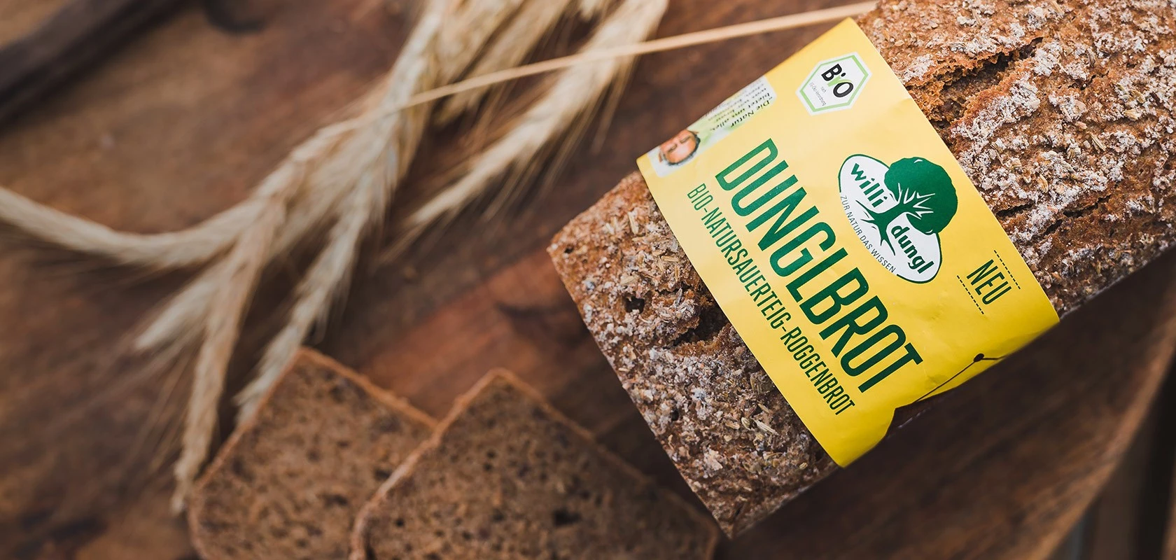 DUNGLBROT Roggenbrot mit gelbem Etikett, geschnitten, auf Holz mit Weizenhalmen; bio-zertifiziert.