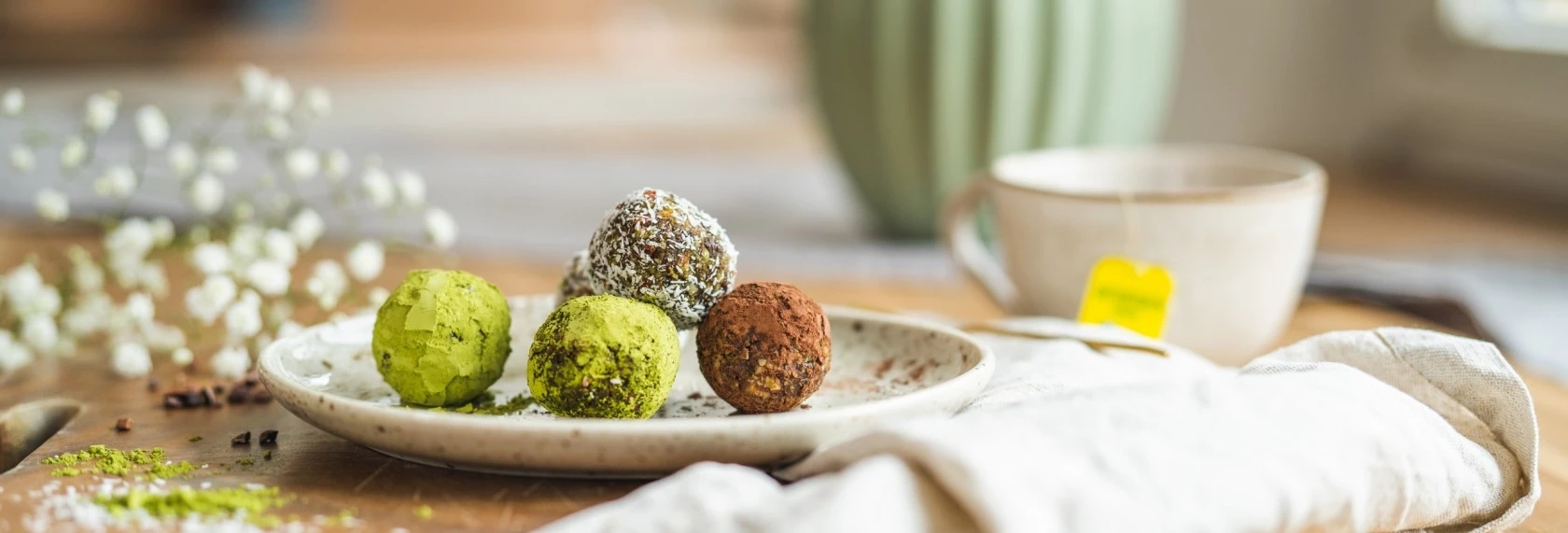 Bunte Trüffel auf einem Teller neben einer Tasse Tee und weißen Blumen im Hintergrund.