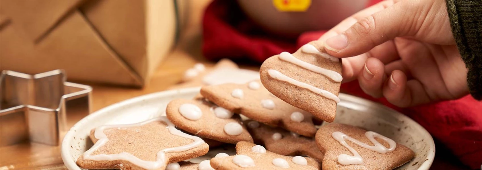 Von Hand Weihnachtsbaumplätzchen von einem Teller mit verschiedenen Weihnachtsplätzchen pflücken, umgeben von festlicher Dekoration.