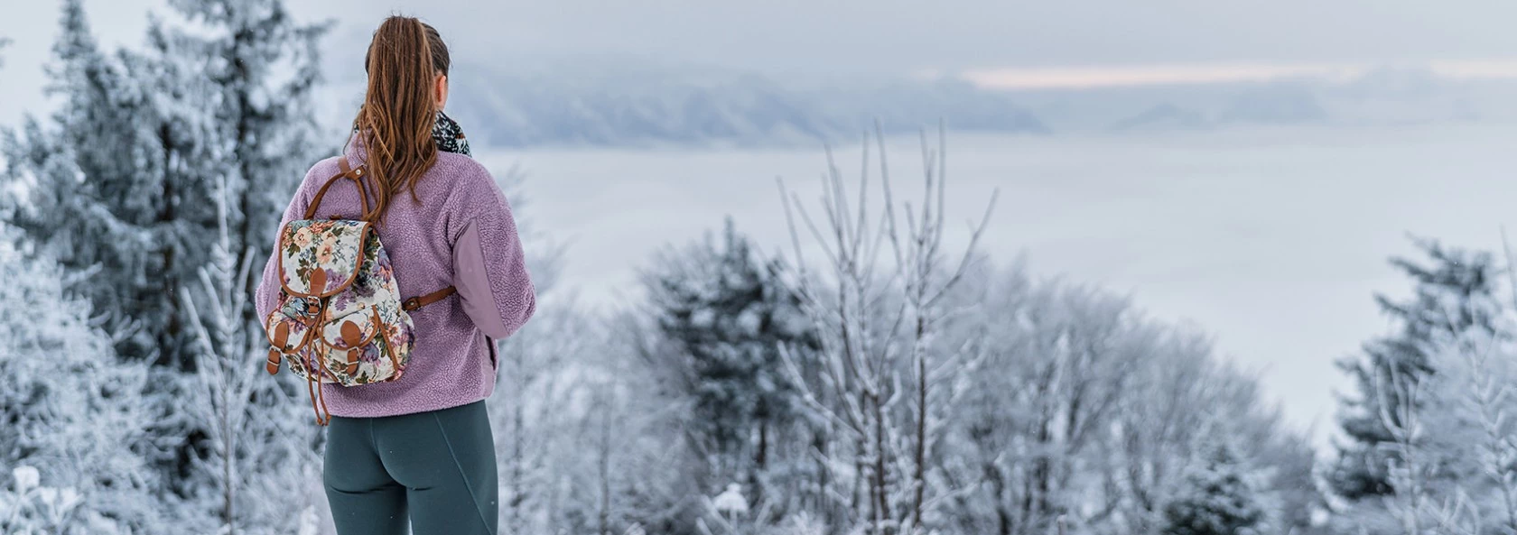 Frau steht mit Sportkleidung vor Winterlandschaft