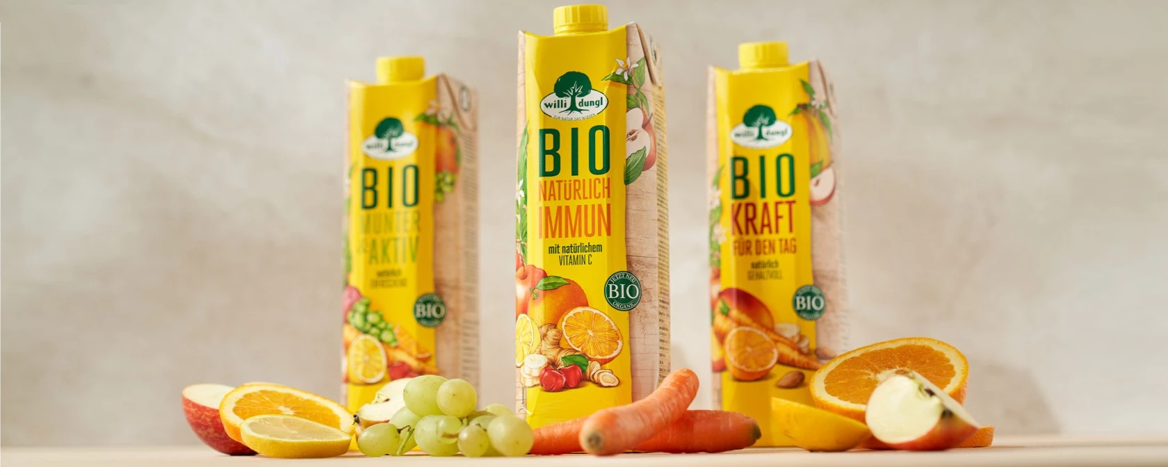 Wild Land-Saftkartons, umgeben von frischen Orangen, Äpfeln, Zitronen, Trauben und Karotten auf dem Tisch.