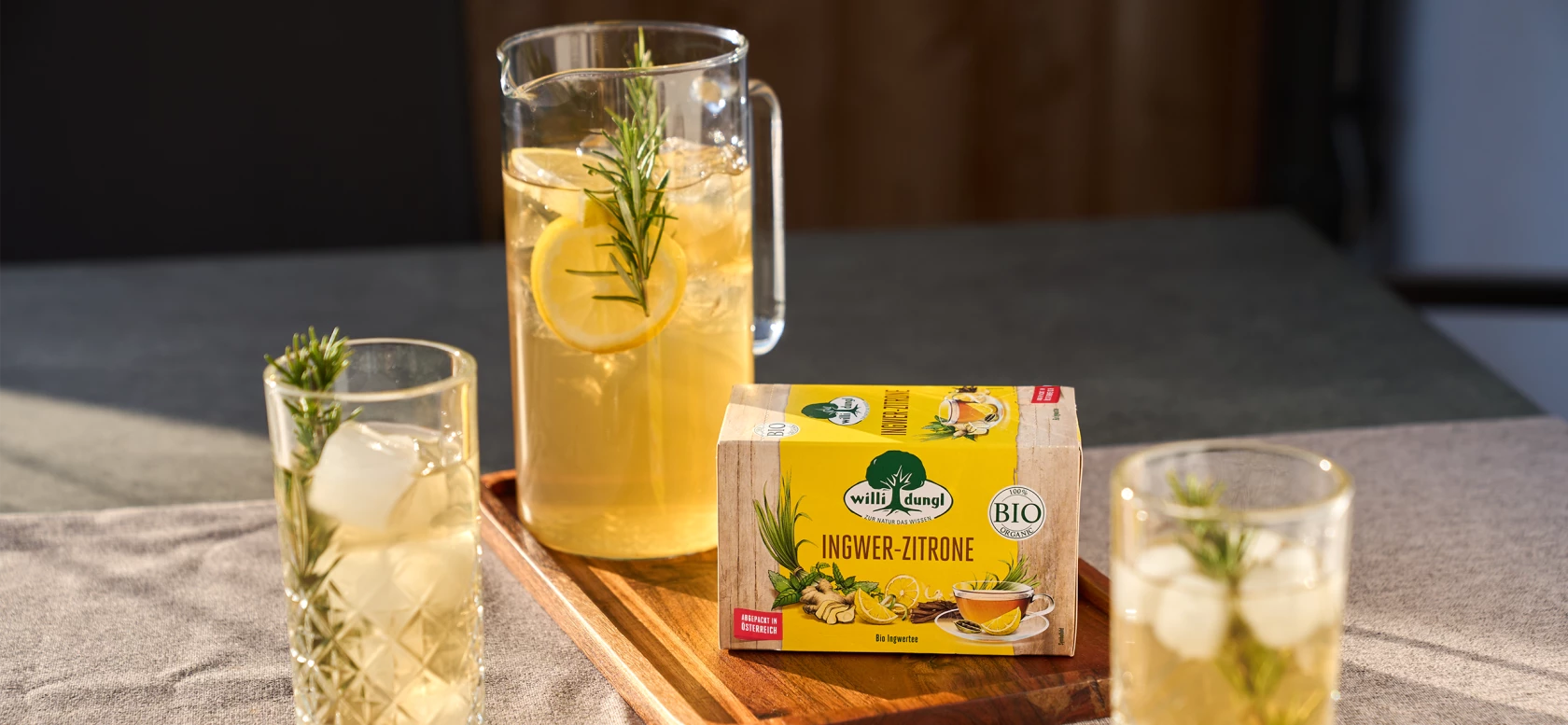 Krug und Gläser mit Zitronen-Ingwer-Tee mit Rosmarin neben Willi Dungl Bio-Teebox.