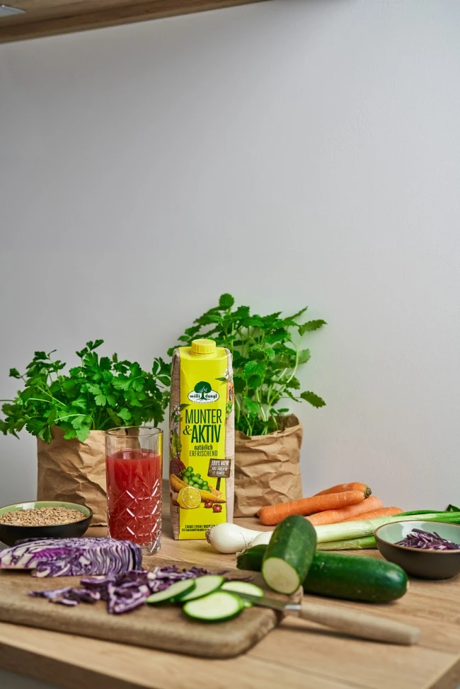 Frisches Gemüse, Kräuter, Getreide und ein Zitronengetränk, angerichtet auf einer hölzernen Küchentheke.