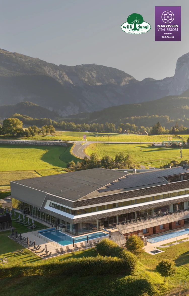 Modernes Resort mit Glasfenstern, Außenpools, grünen Feldern und Bergen, klarem Himmel, zwei Logos oben links.